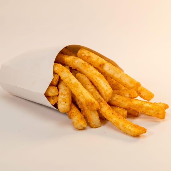 Seasoned french fries spilling out of a white paper container onto a light background.