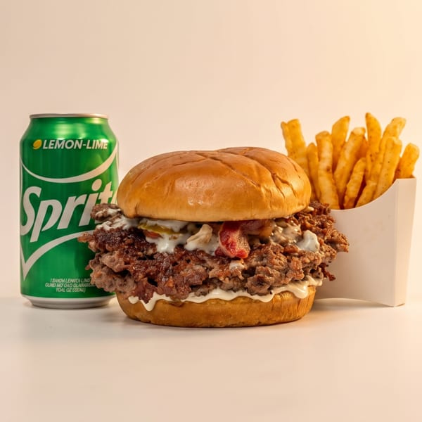 A Sprite can, a cheesesteak sandwich with sauce and bacon, and a side of fries.