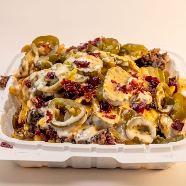 Loaded fries with melted cheese, ground beef, jalapeños, and bacon bits in a white takeout container.