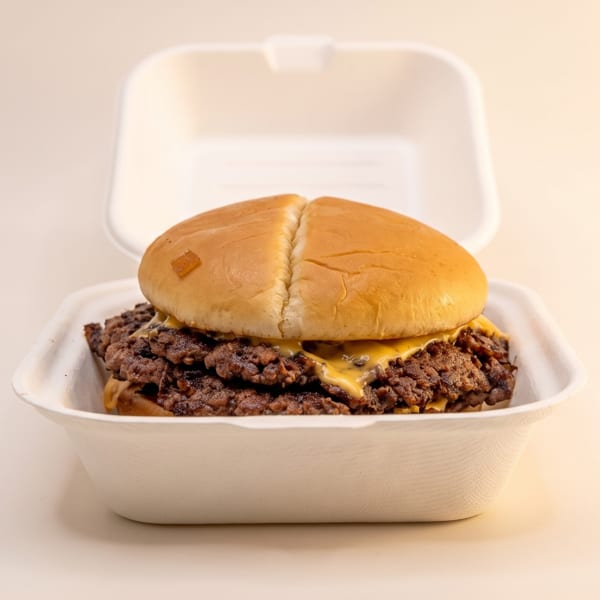 A double smash burger with melted cheese in a white takeout container, on a light background.